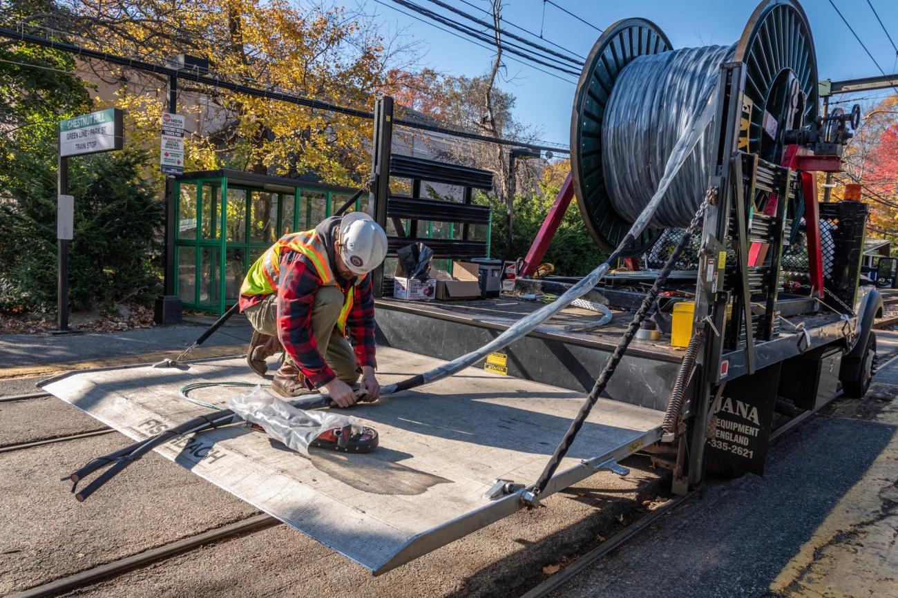 A crewman unwinds signal cable from a large spool, at Chestnut Hill on the Green Line D branch.