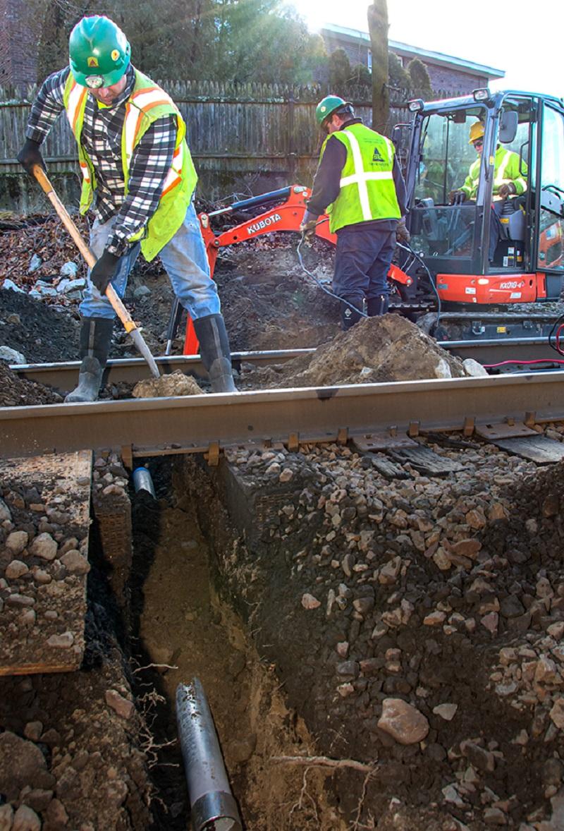 A crew excavates underneath the track where signal communication line will be installed as part of the PTC upgrades on the Franklin Line of the Commuter Rail (January 2020)