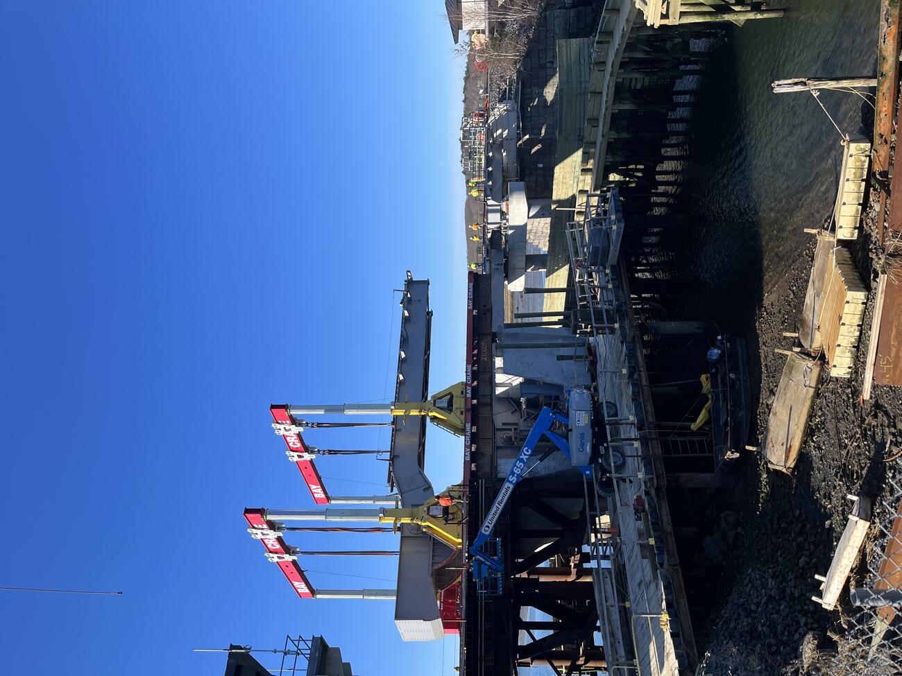 A large gantry crane lifts the new bascule span off the self-propelled modular transporters 