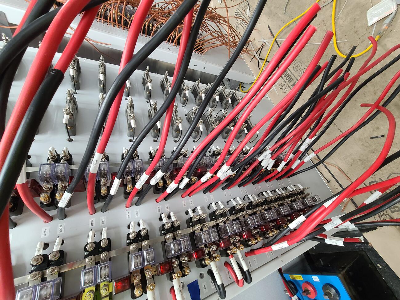 Red and black cables stick out of a grey metal wall full of circuitry during the installation of track circuits inside a signal house at North Station.