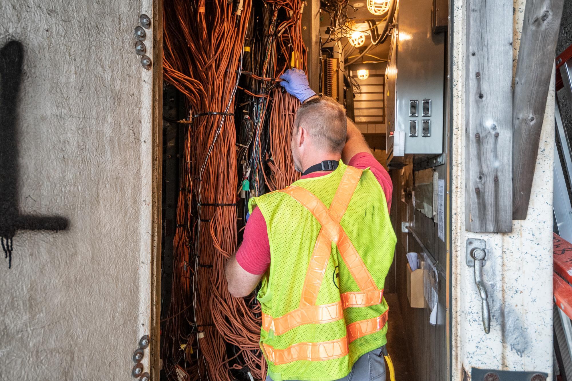 A worker in a neon vest handles wiring during signal repair at the JFK/UMass signals bungalow.