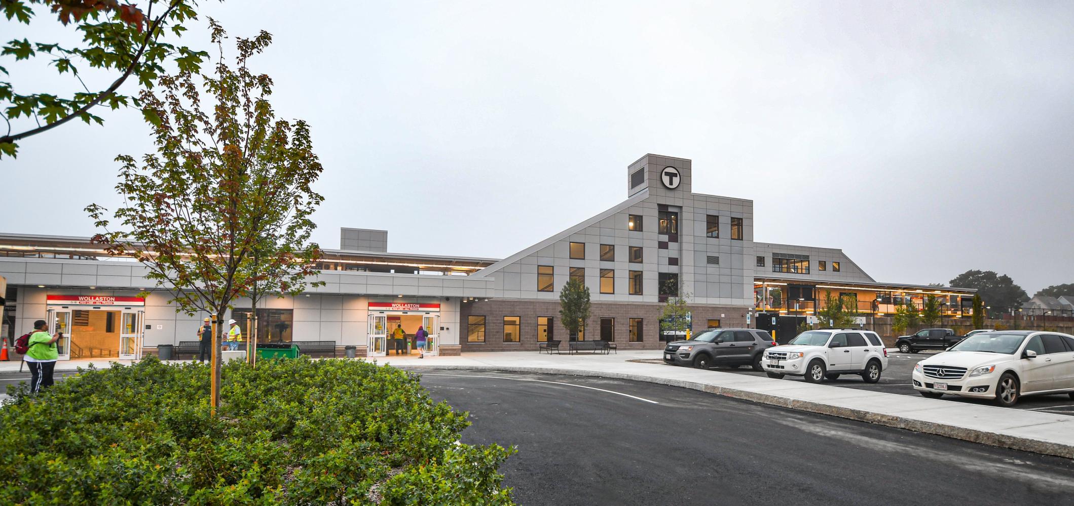 The building facade and entrances of newly renovated Wollaston Station, with the platform to the right, viewed from the parking lot.