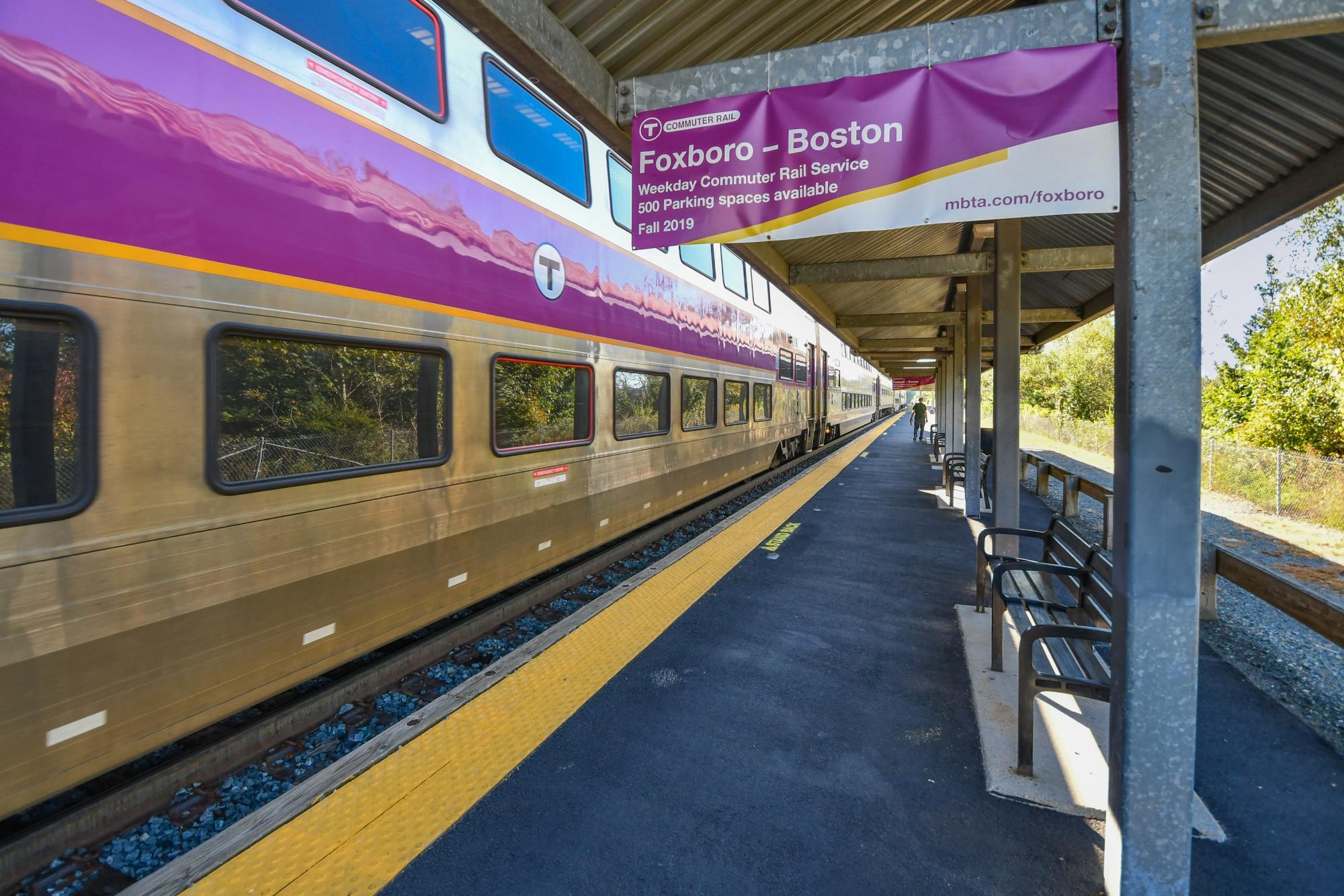 A Commuter Rail train at Foxboro Station's platform, with an advertisting sign for the Foxboro - Boston weekday pilot in the foreground.