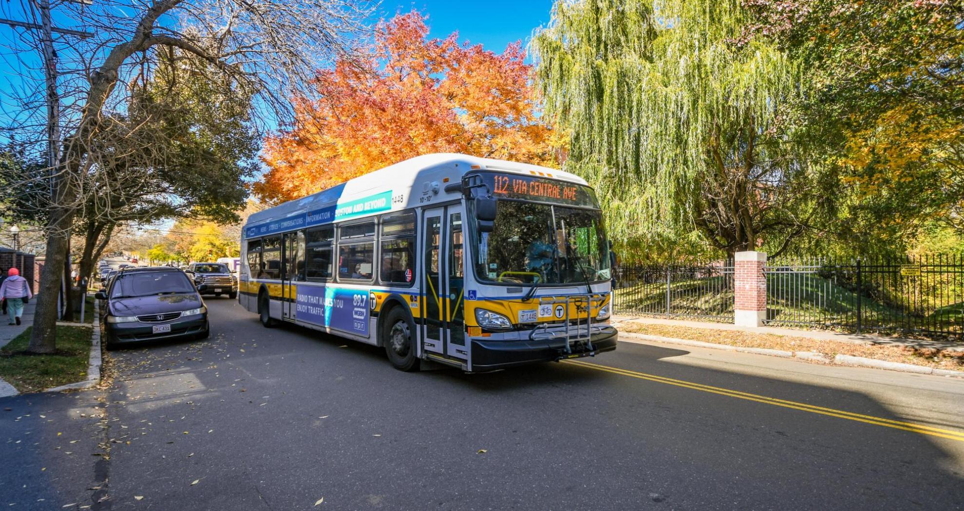 Route 112 bus with a headsign that says "Via Central Ave" travels through Chelsea, with fall foliage in the background