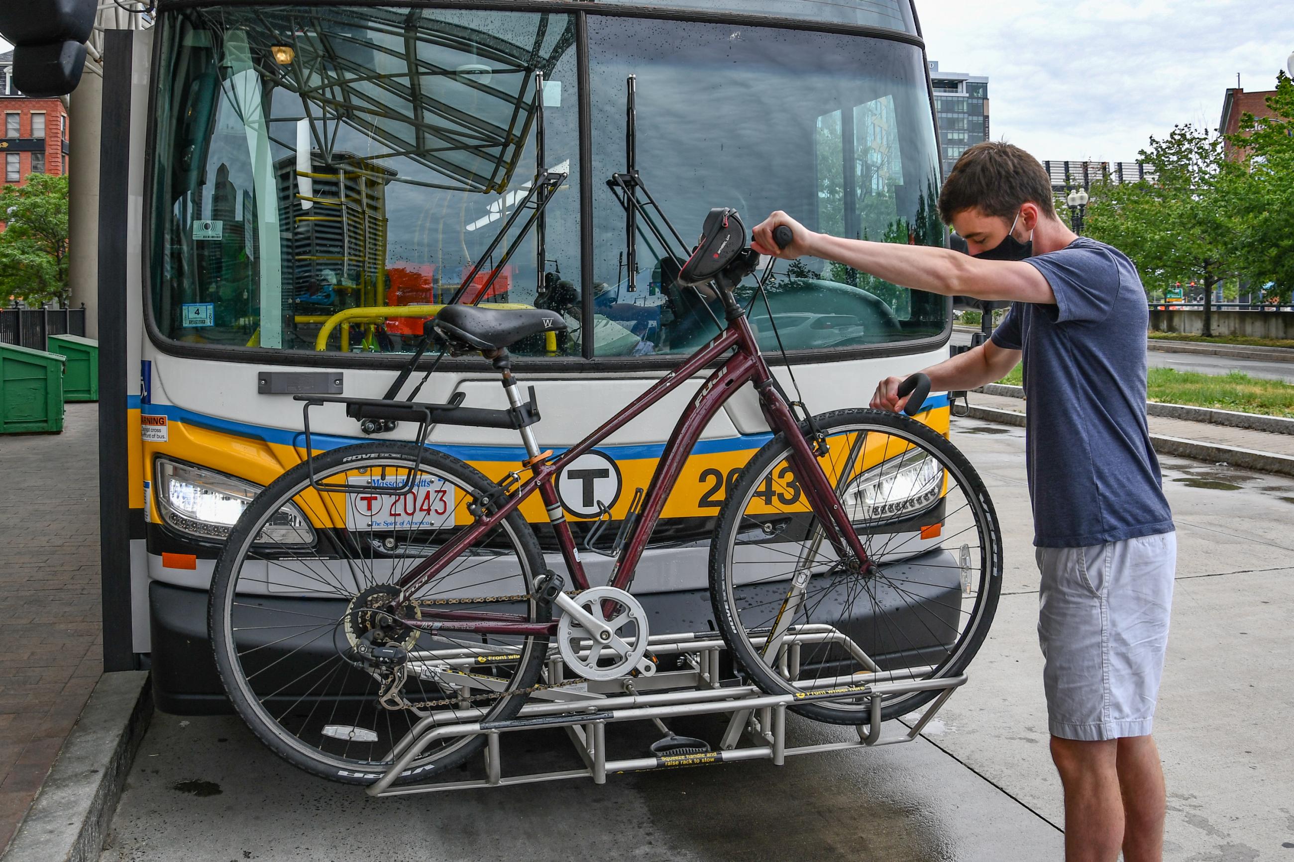 A person secures a bicycle on the bike rack on the front of a bus at Haymarket station